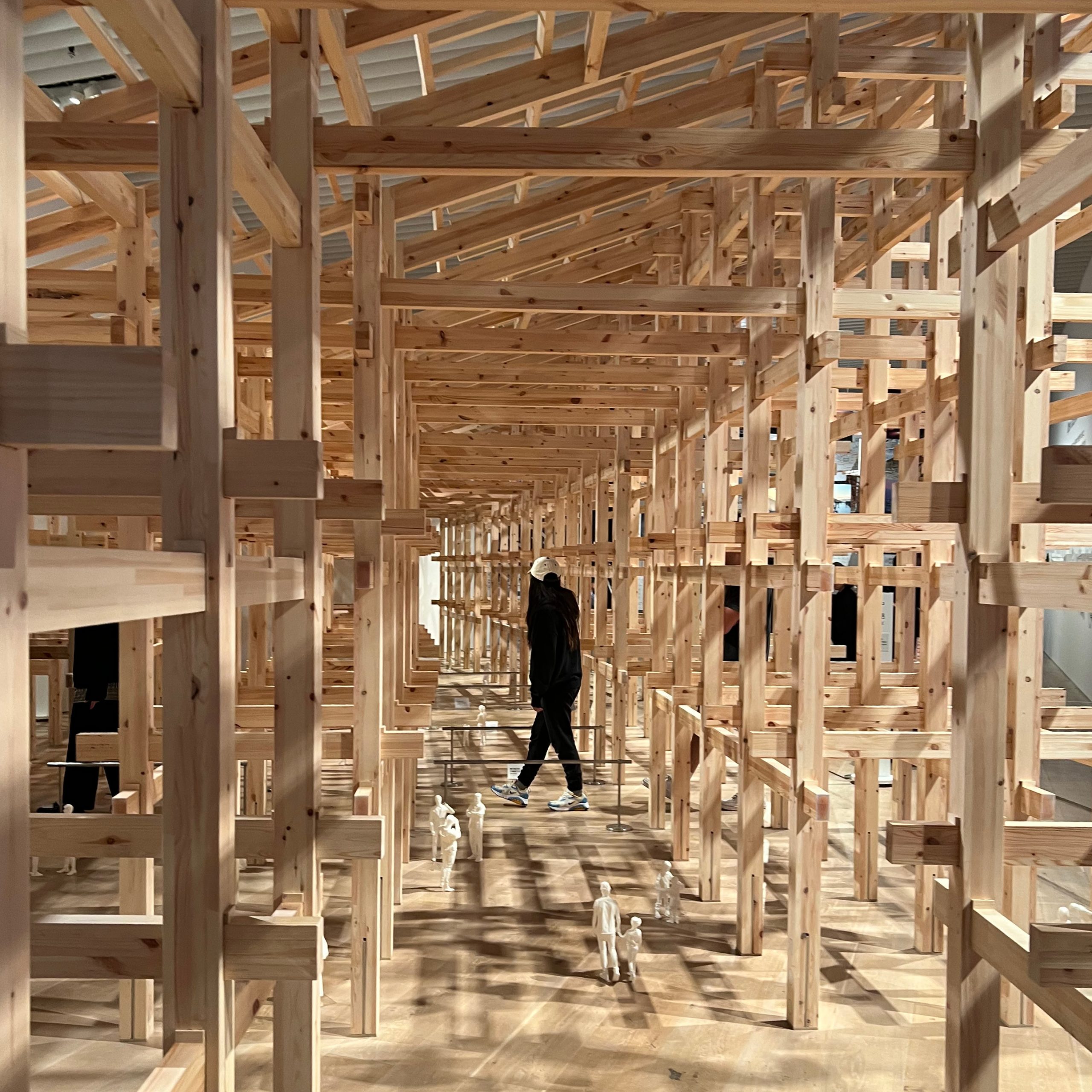 A 1:5 scale timber model of the Grand Ring, on display at the Sou Fujimoto Mori Art Museum exhibition in Tokyo, showing a visitor walking through the column and beam joinery.