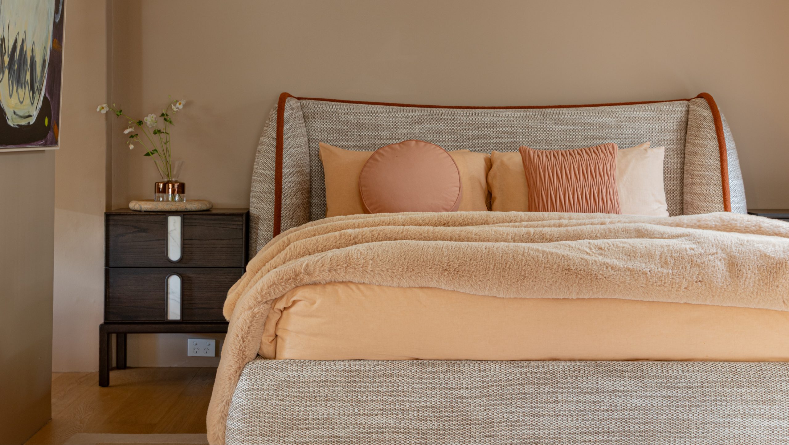 Bedroom styled with an upholstered bed in grey fabric and tan leather trim, orange and pink cushions, in the Zuster Furniture Sydney Showroom